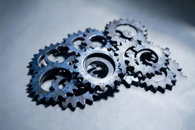 Um conjunto de engrenagens de metal interligadas de tamanhos variados, com algumas peças em movimento, em uma superfície cinza, luz forte vinda de cima, detalhe, sem pessoas.