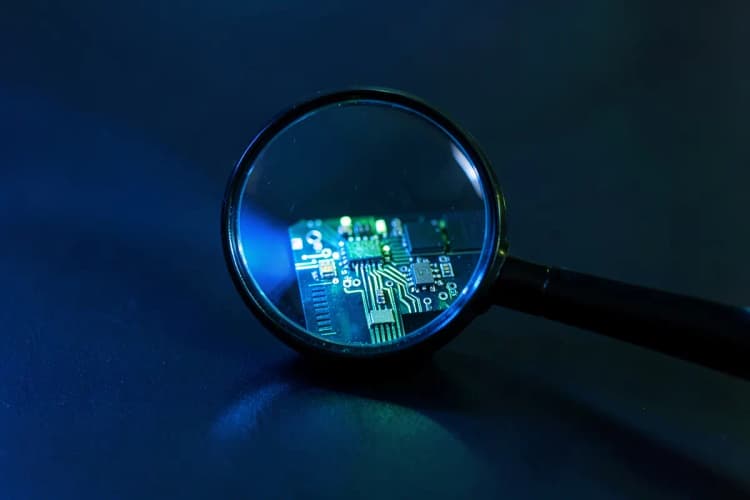 Uma lupa examinando um pequeno pedaço de circuito eletrônico em uma superfície escura, luz focada vinda da esquerda, detalhe, sem pessoas.