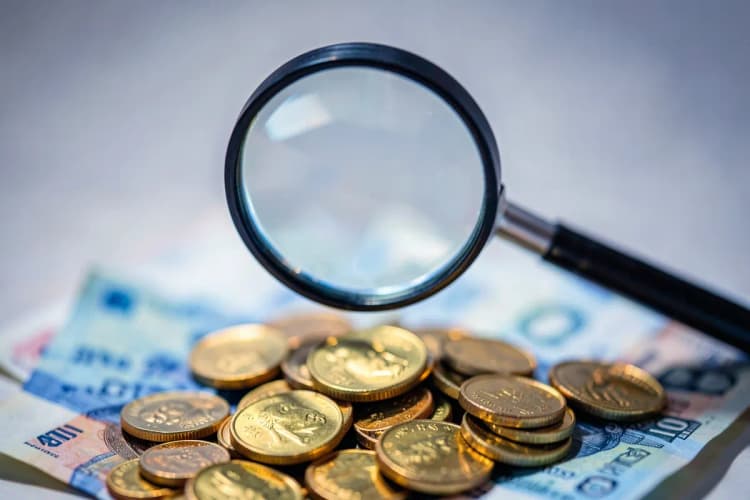 Uma lupa examinando atentamente uma pilha de moedas de ouro e notas de dinheiro.