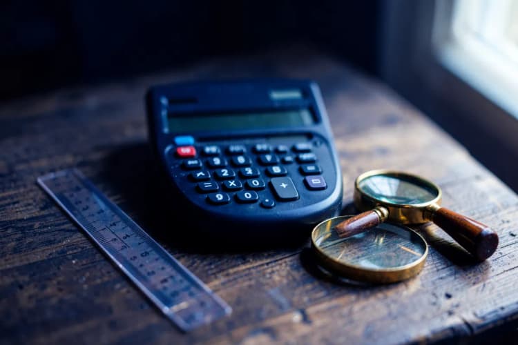 Uma coleção de ferramentas de escritório como calculadora, régua e lupa dispostas sobre uma mesa de madeira.
