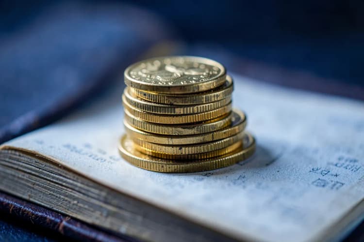Moedas de ouro empilhadas em cima de um livro aberto com uma lupa sobre ele